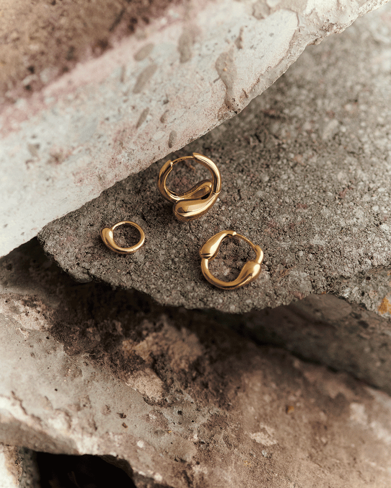 Sculptural oval huggie hoops with asymmetric design featuring elongated drop-shaped motifs